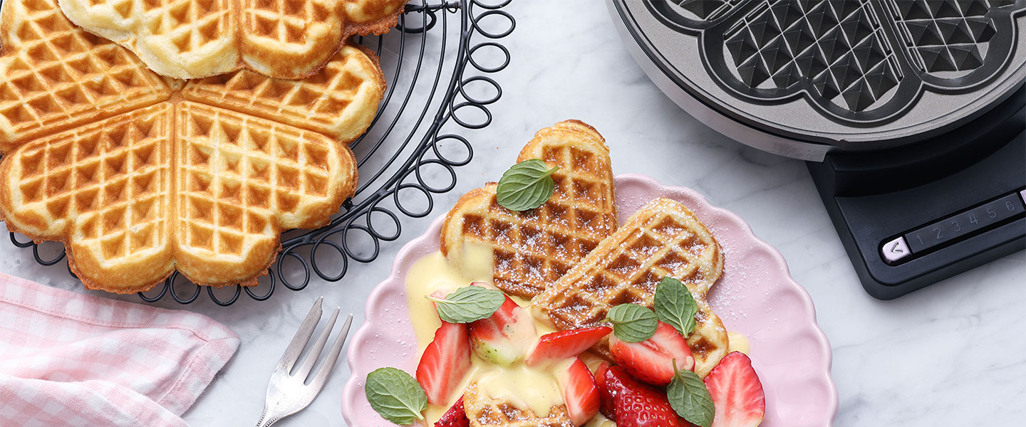 Herzförmige Waffeln mit Erdbeeren und Minze auf einem rosa Teller, Waffeleisen