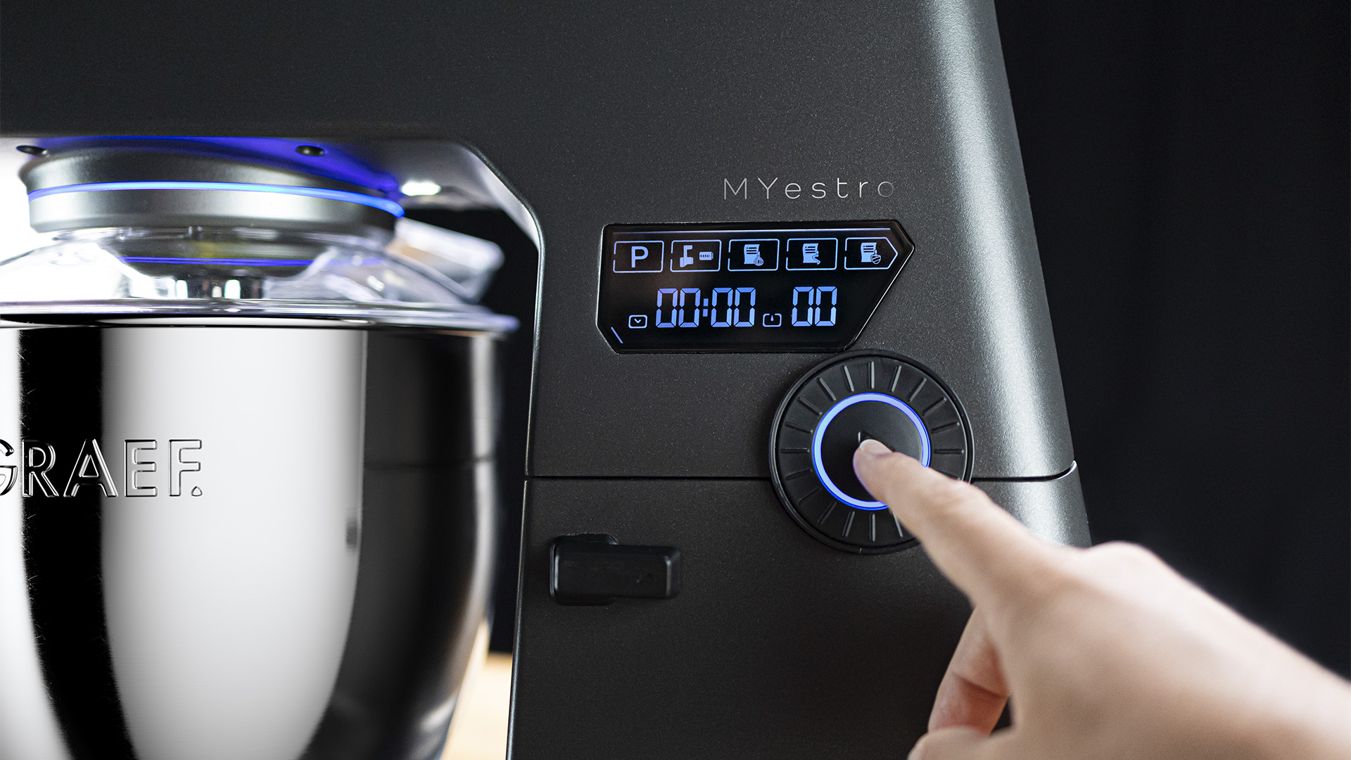 Robot de cuisine avec écran numérique et molette, doigt touchant la molette