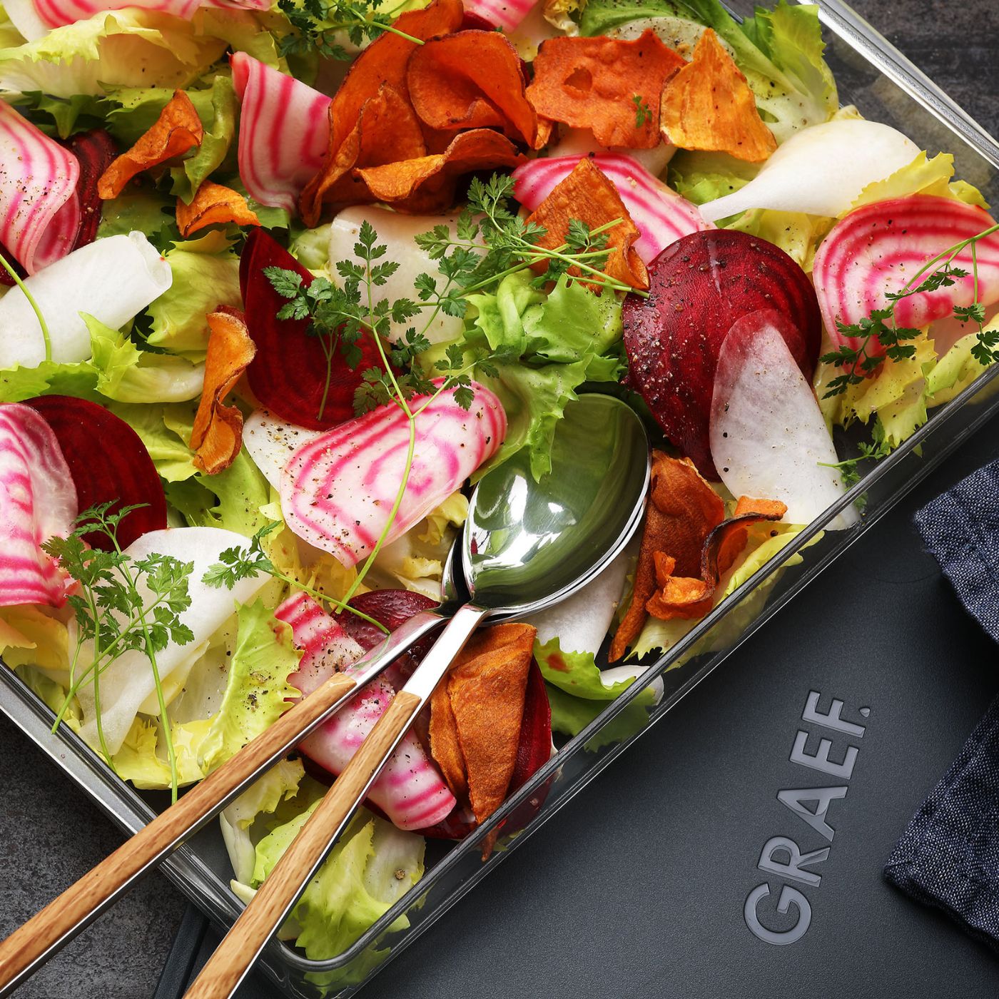Close-up of salad with vegetables and chips in a bowl with cutlery and GRAEF logo.