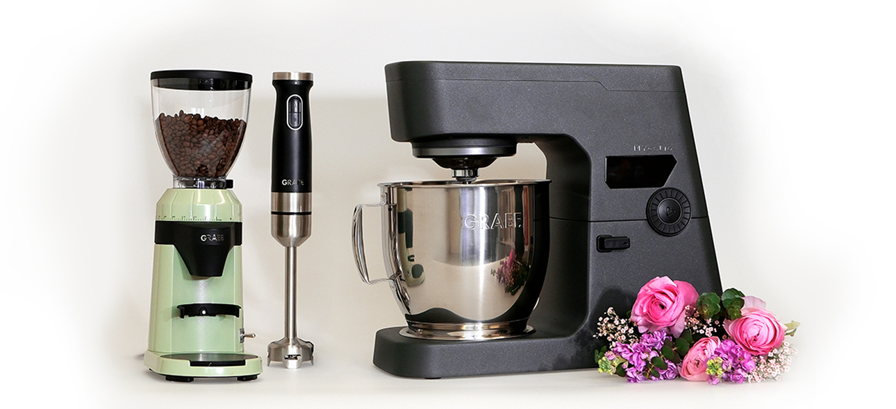 Kitchen appliances: coffee grinder, immersion blender, and stand mixer with flower arrangement.