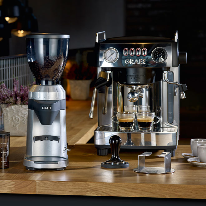 Kaffeemaschine und Kaffeemühle auf einer Holzoberfläche mit Zubehör.
