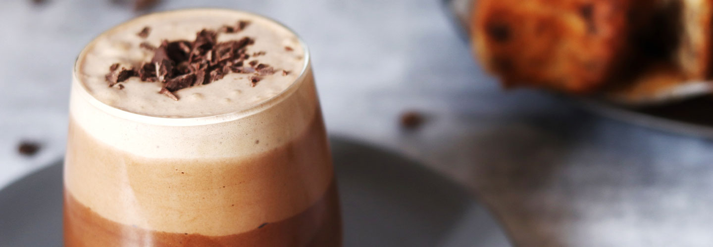 Boisson au café avec copeaux de chocolat, servie dans un verre sur une assiette.