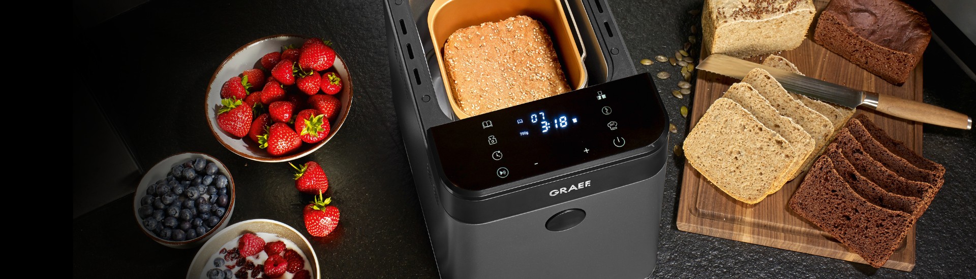 Brot, Erdbeeren und Blaubeeren neben einem Brotbackautomaten