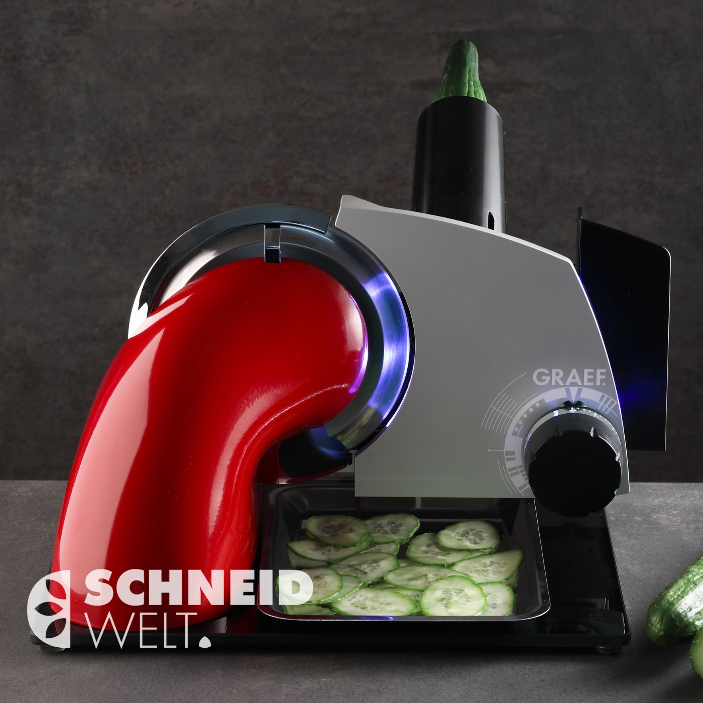 Gemüseschneider mit Gurken, die in Scheiben geschnitten werden, auf einem grauen Hintergrund.