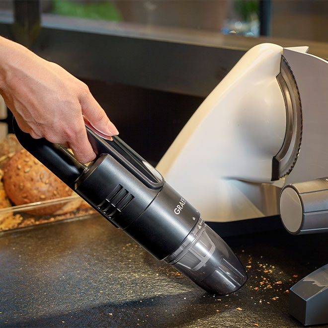 Hand hält schwarzen Staubsauger, der Krümel von einer schwarzen Oberfläche aufsaugt.