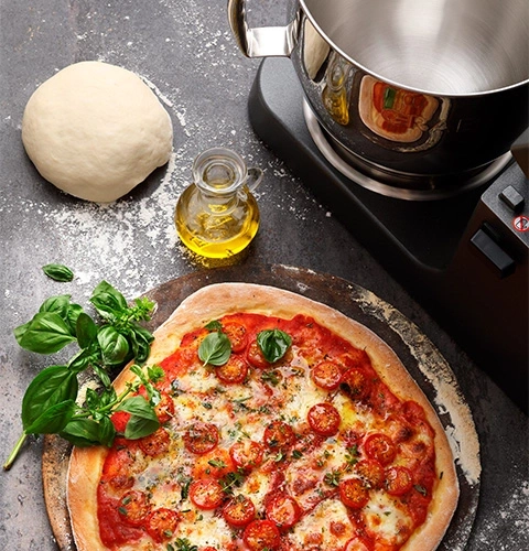 Pizza with tomatoes, basil, and ingredients on a table