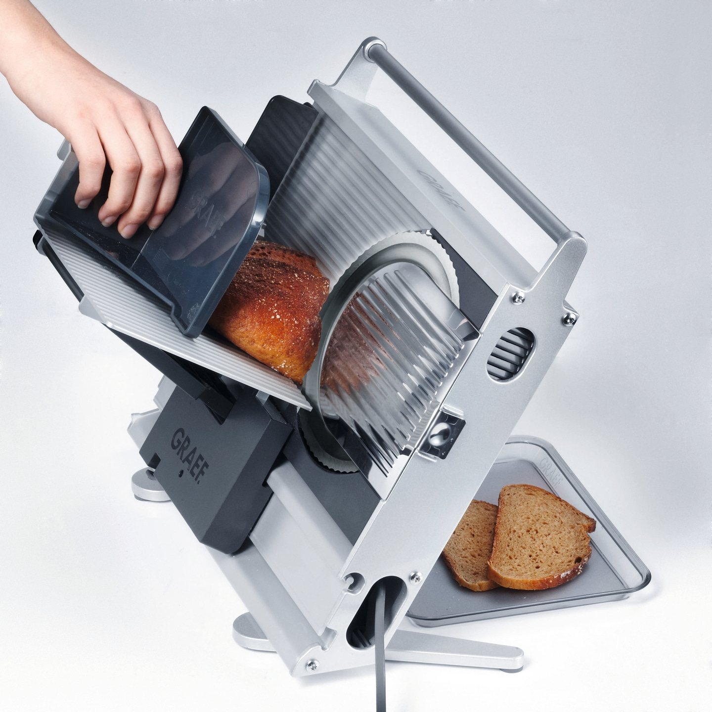 Bread slicer with bread and sliced pieces, grey machine, hand