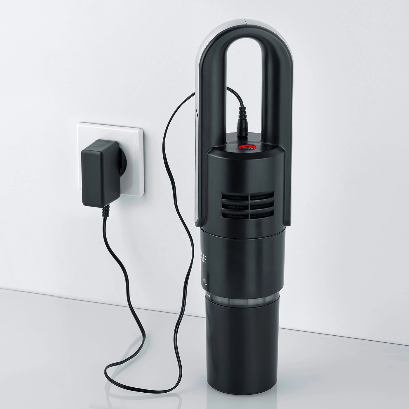 Aspirateur noir avec chargeur mural, prêt à charger et à nettoyer la surface.