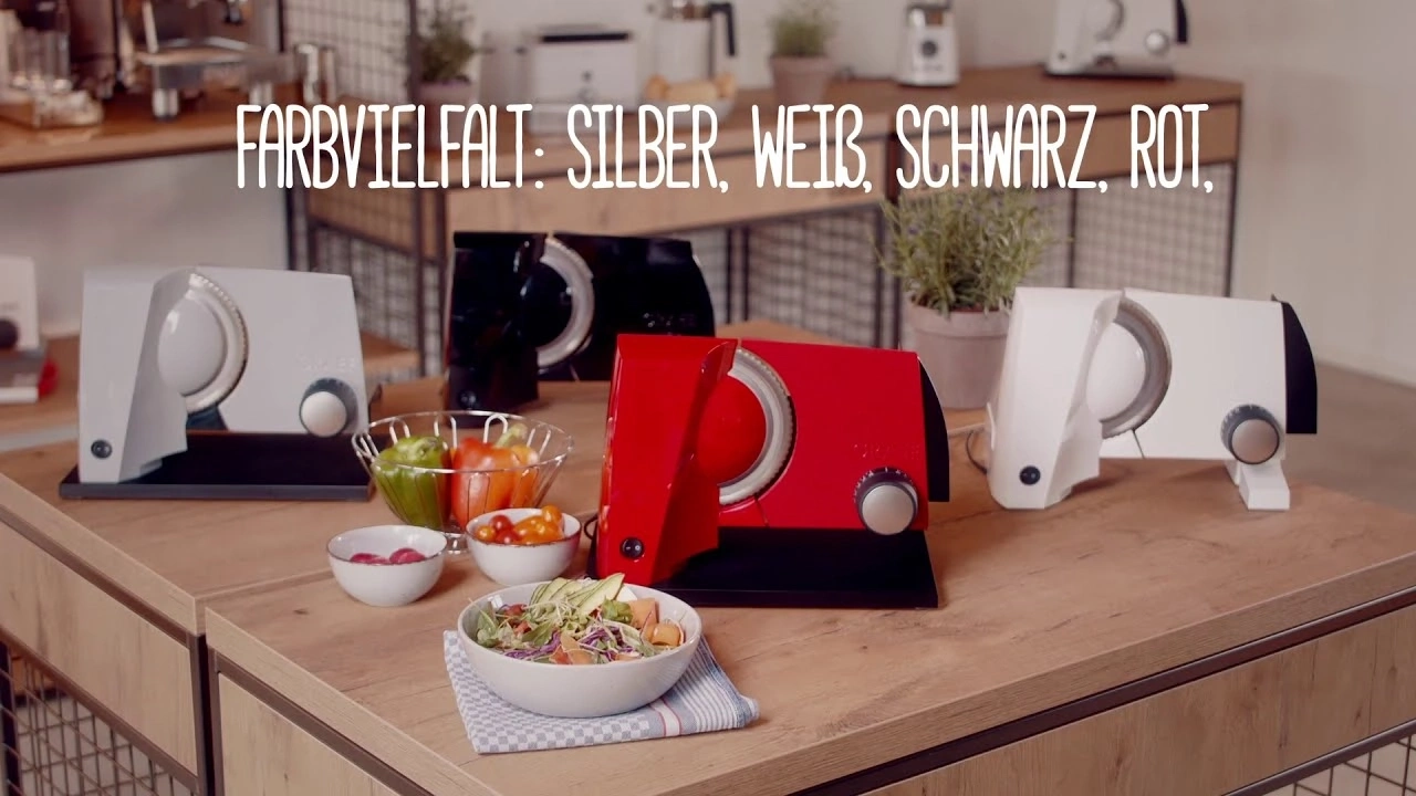Gemüseschneider in Silber, Weiß, Schwarz und Rot auf Holztisch mit Gemüse und Salat.