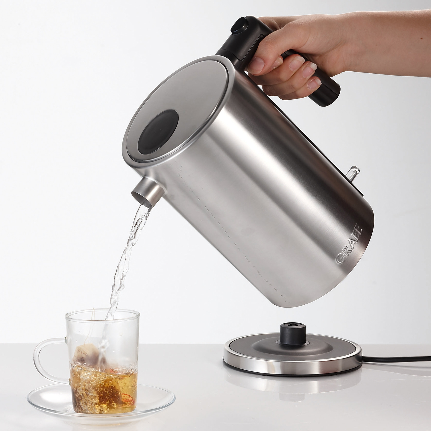 Eine Person gießt heißes Wasser aus einem Wasserkocher in eine Teetasse.