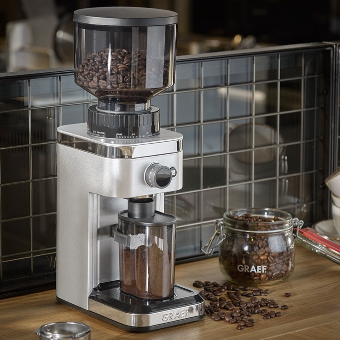 Moulin à café avec grains et bocal en verre sur surface en bois