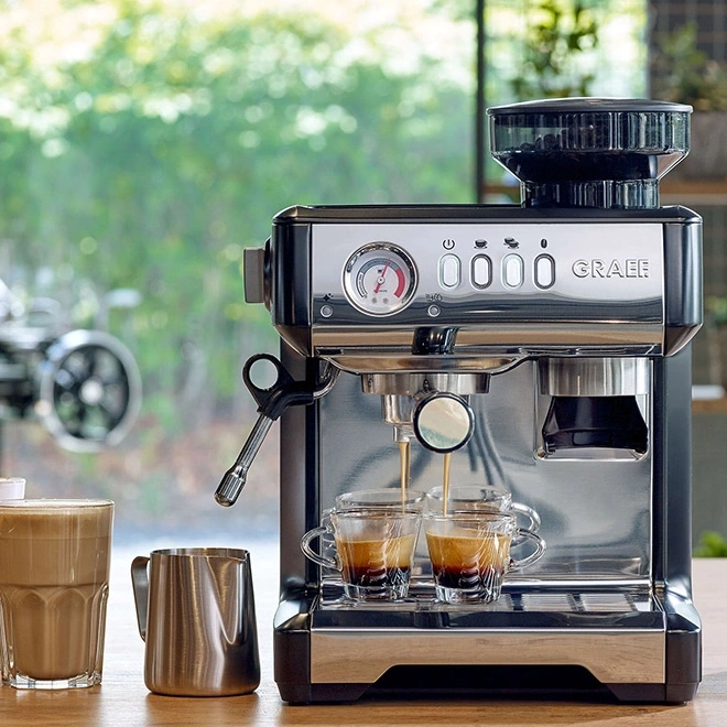 Machine à expresso avec deux tasses, pichet à lait et un verre de café