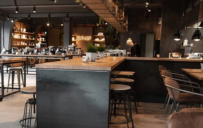 Intérieur d'un café avec un bar, des tables et des chaises, une personne et des plantes.