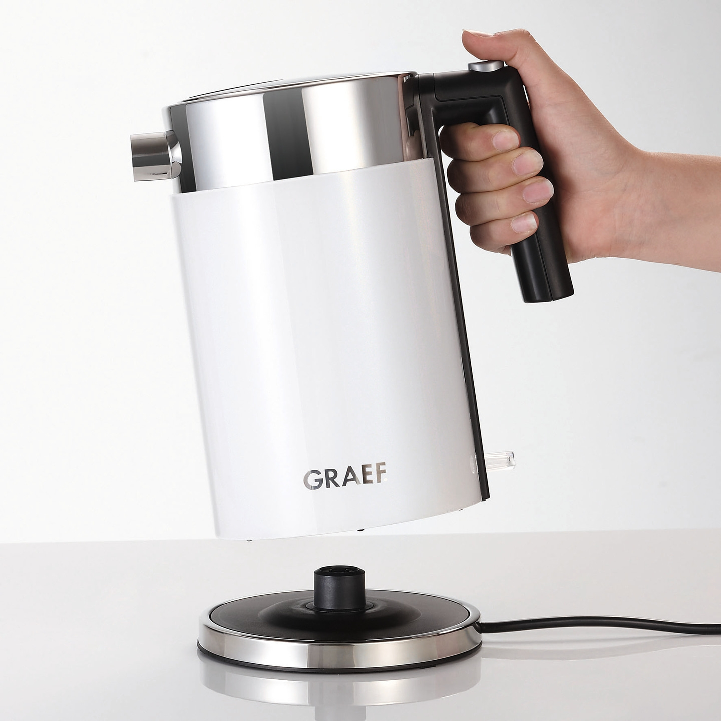 Weißer Wasserkocher mit schwarzem Griff und Basis, gehalten von einer Hand.
