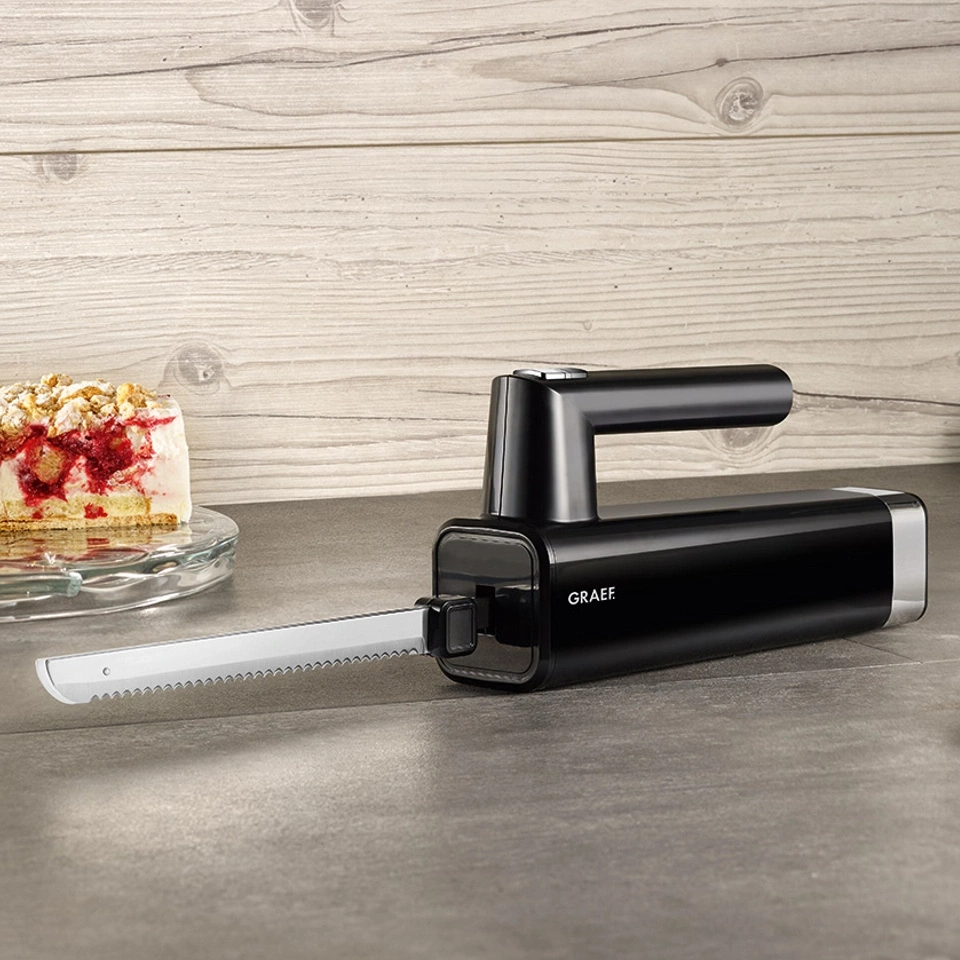 Black electric knife with cake in the background on a gray surface.