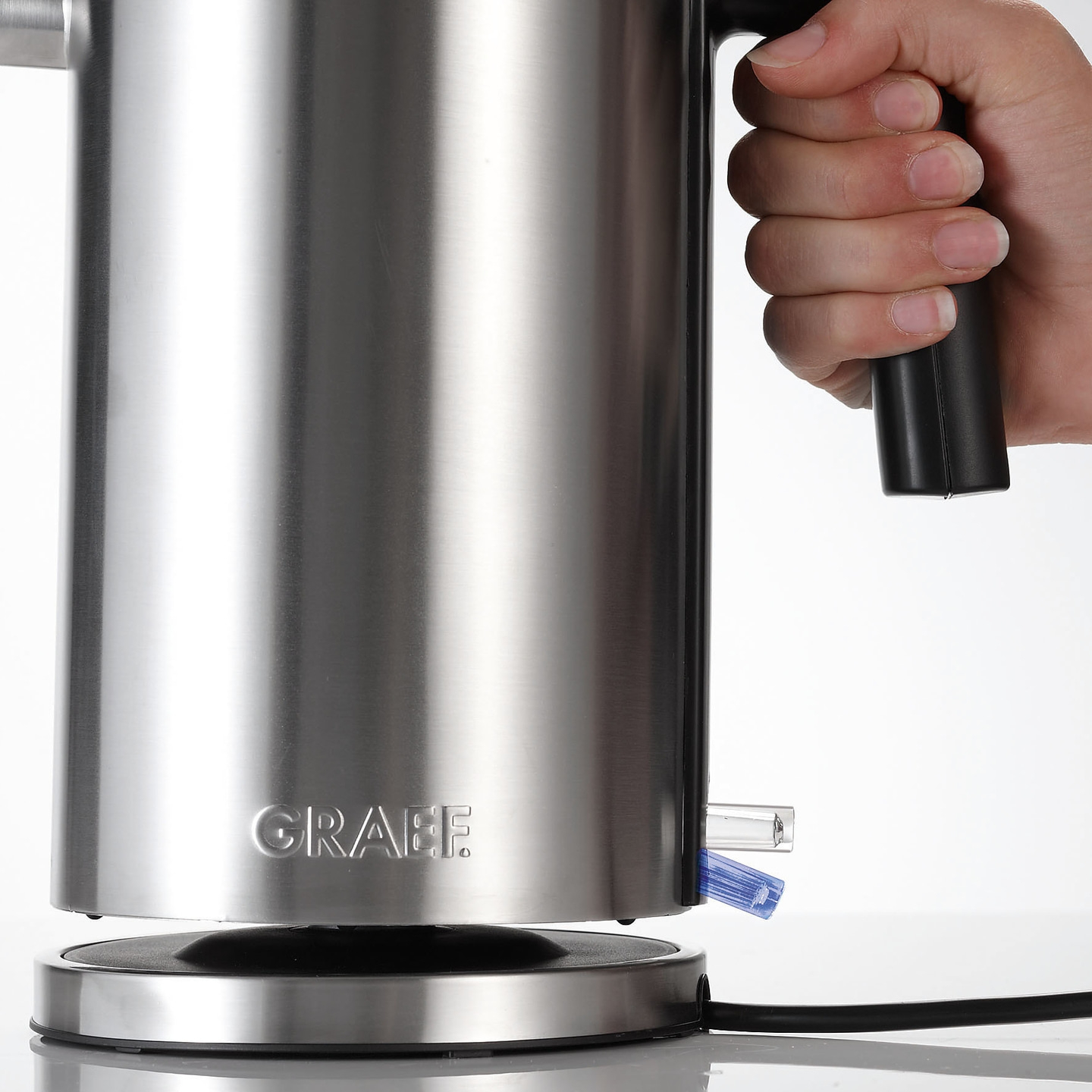 Edelstahl-Wasserkocher mit Griff und Hand, die ihn hält, auf weißem Hintergrund.