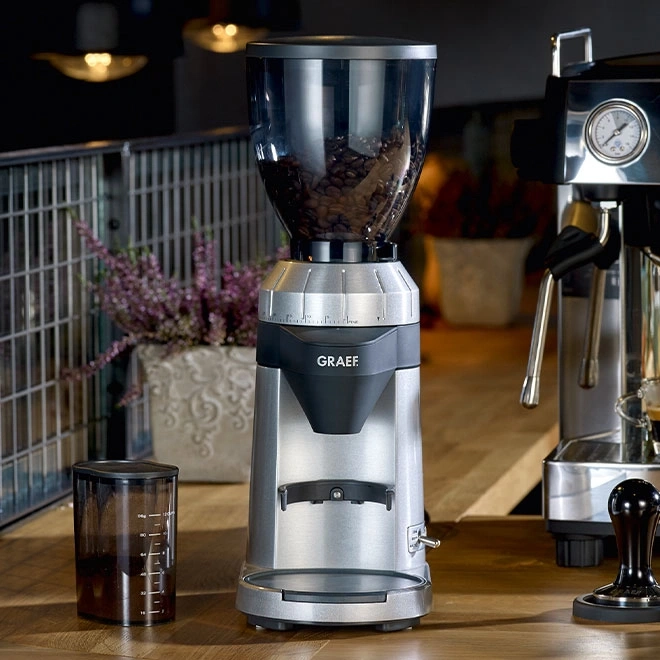 Kaffeemühle mit Bohnen, neben einer Espressomaschine und einem Behälter.