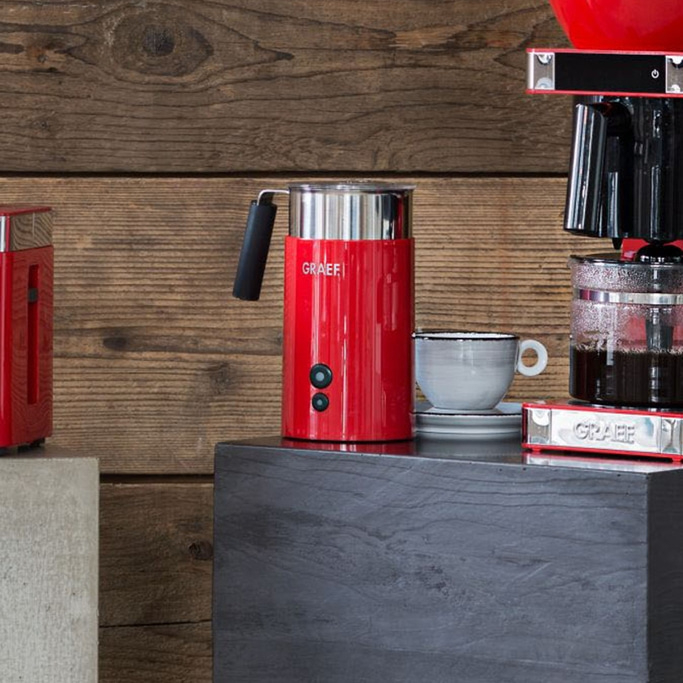 Red coffee machine and milk frother on a table with a cup and saucer