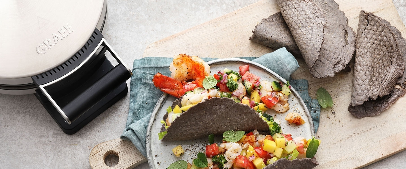 Garnelen-Tacos mit Gemüse auf einem Teller, daneben ein Tortilla-Maker und Tortillas.