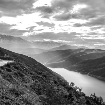 Landschaftsfoto in Schwarzweiß: Berge, See und Wolken am Himmel.