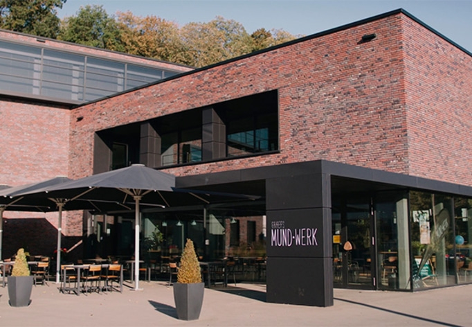 Gebäude mit Ziegelmauerwerk, Restaurant mit Sonnenschirmen und Schild.