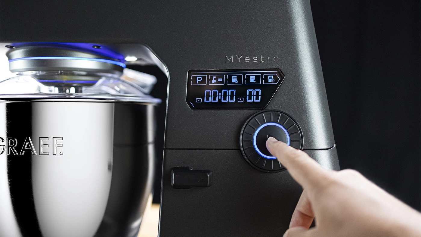 Robot de cuisine avec écran numérique et molette, doigt touchant la molette