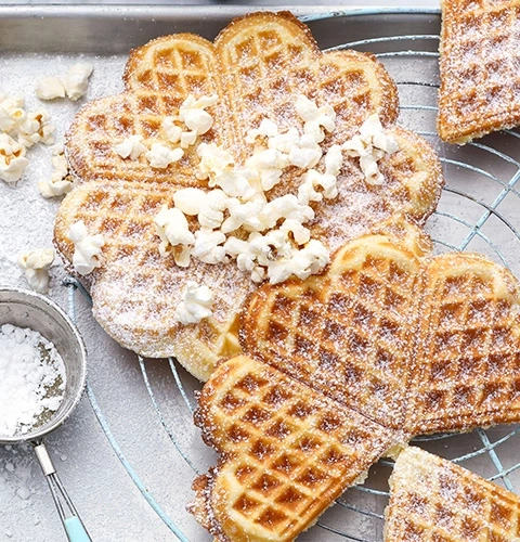 Herzförmige Waffeln mit Popcorn und Puderzucker, auf einem Rost.