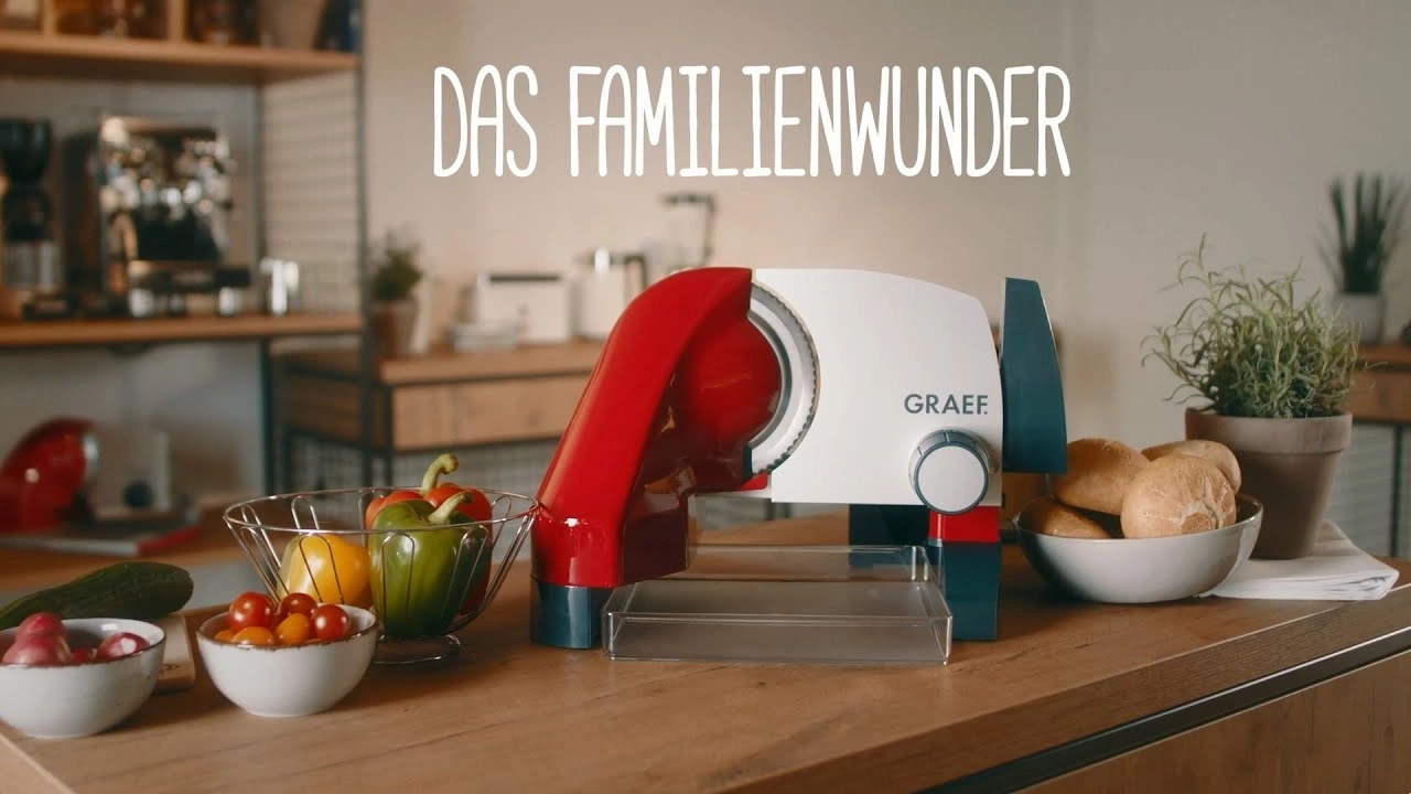 Küchenszene mit Aufschnittmaschine, Gemüse und Brötchen auf einer Holzoberfläche.