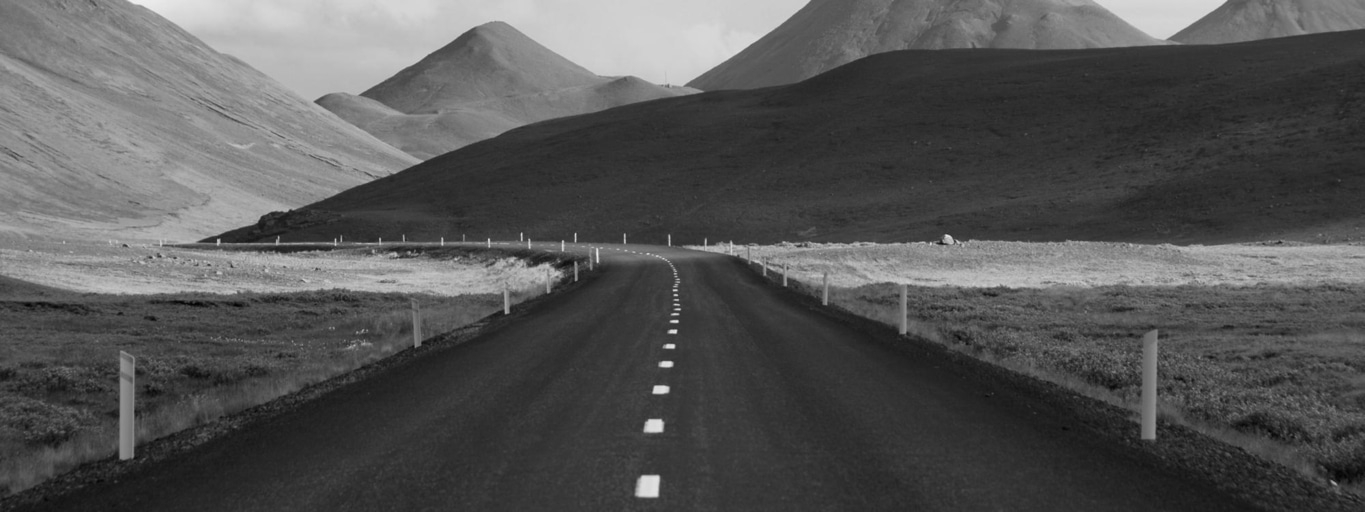 Schwarzweiß-Landschaft mit Straße, Bergen und Himmel. Ruhige, natürliche Szene.
