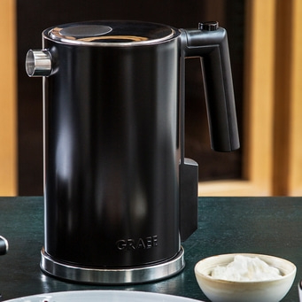 Black electric kettle with handle and logo on a table top.