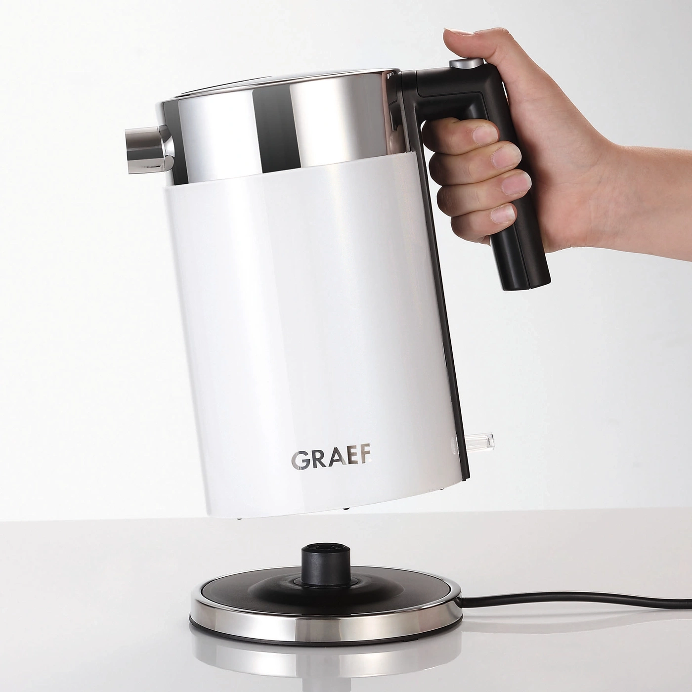 Weißer Wasserkocher mit schwarzem Griff und Basis, gehalten von einer Hand.
