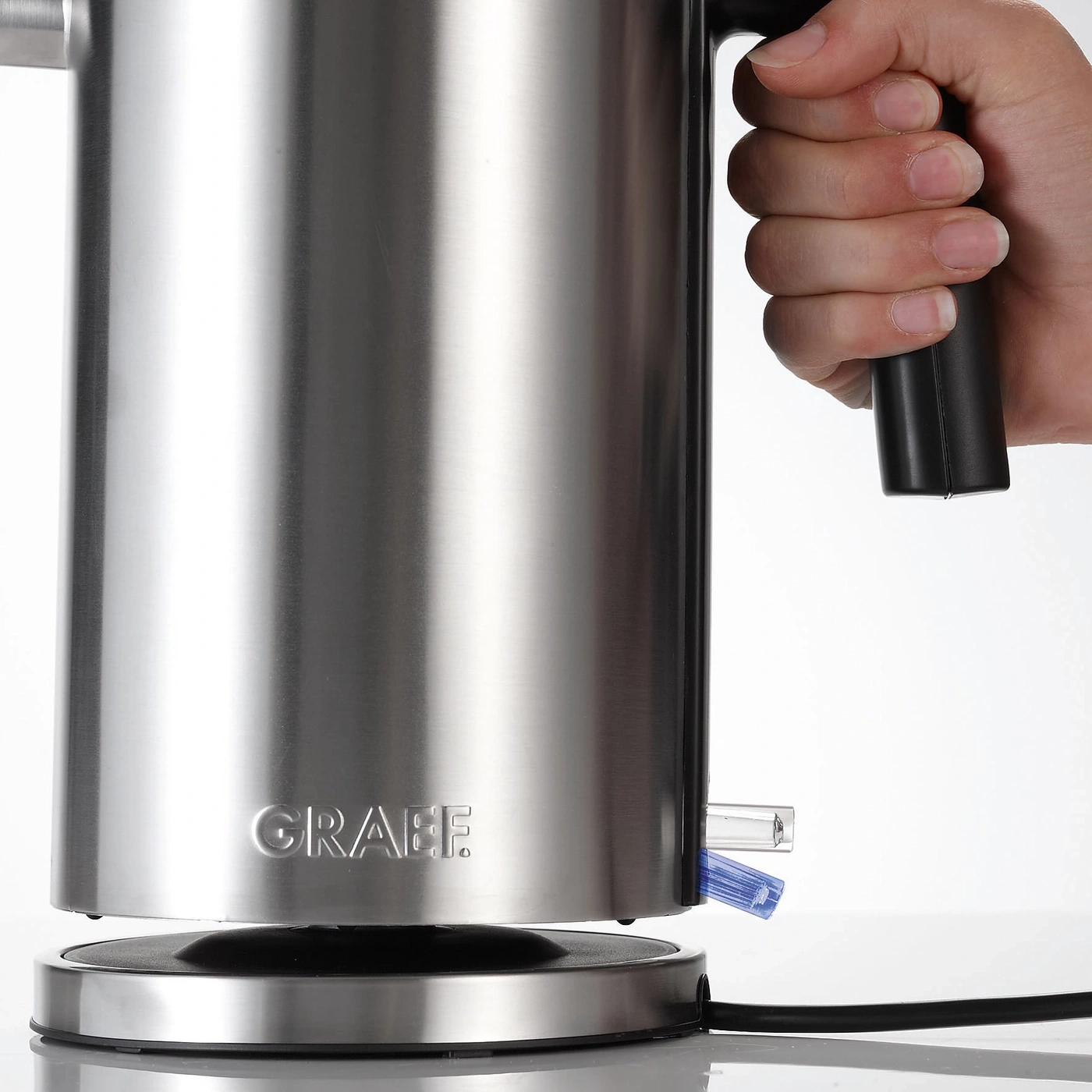 Edelstahl-Wasserkocher mit Griff und Hand, die ihn hält, auf weißem Hintergrund.