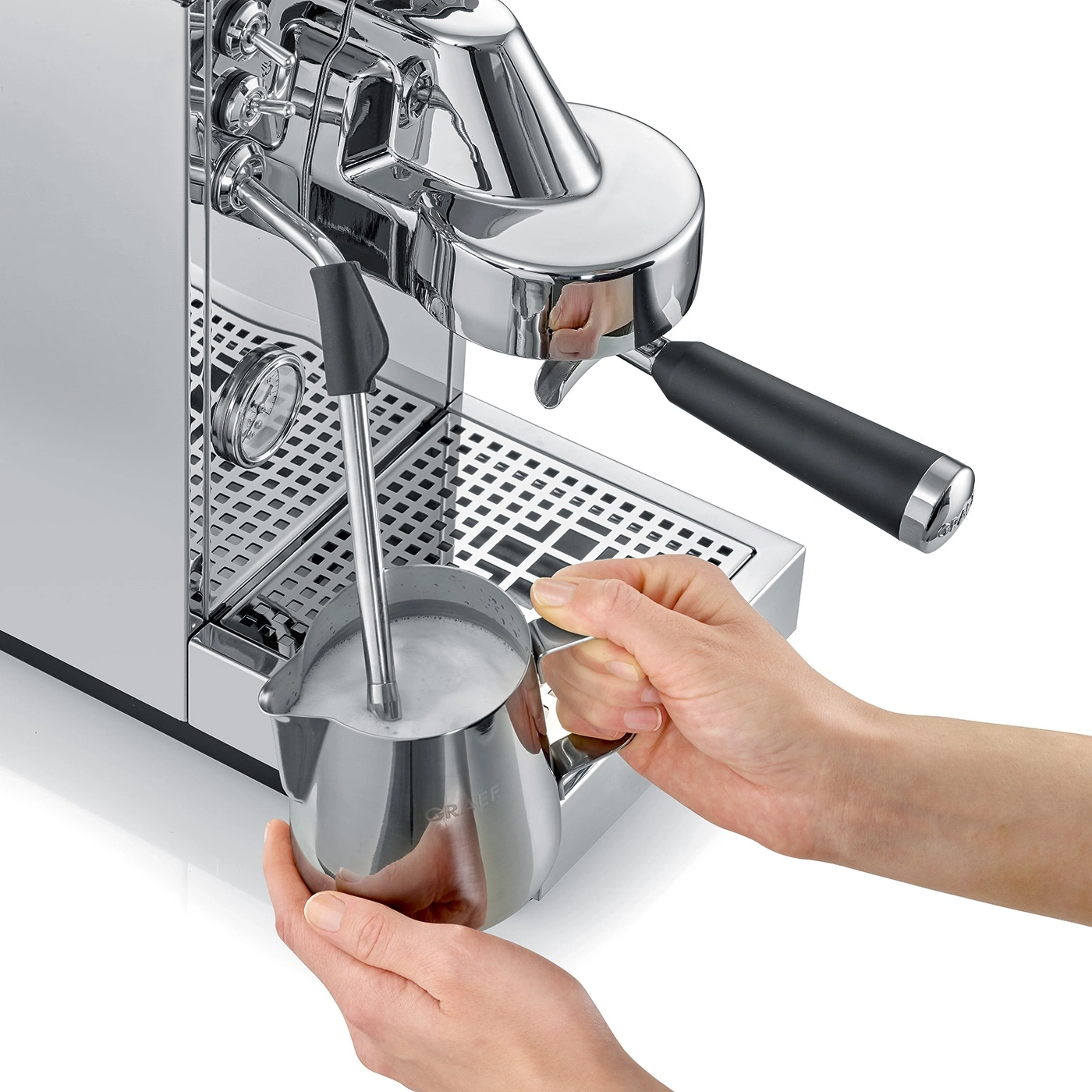 A person frothing milk in a metal pitcher with an espresso machine.