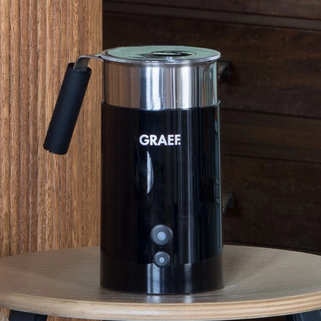 Schwarzer Milchaufschäumer mit GRAEF-Logo auf einem Tisch vor Holz