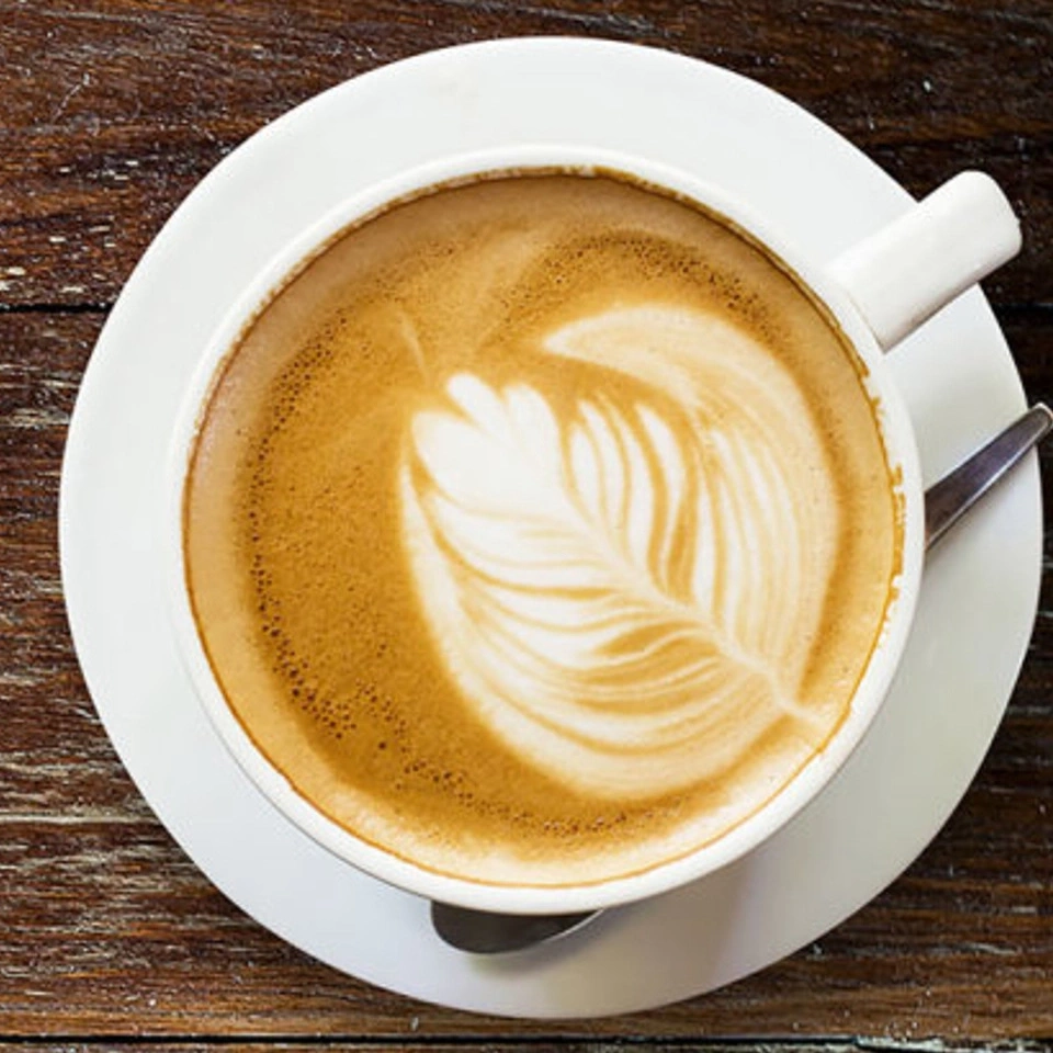 Kaffee mit Latte Art auf einem Unterteller mit Löffel auf Holz
