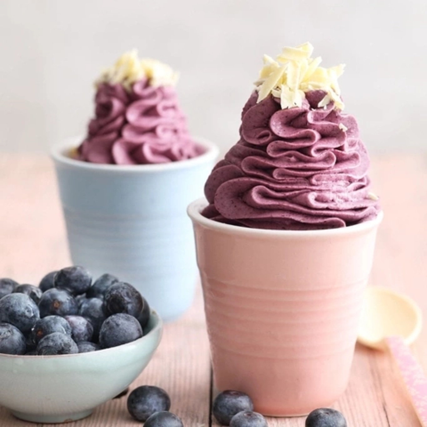 Two cups of blueberry cream with blueberries in a bowl and some on the table.