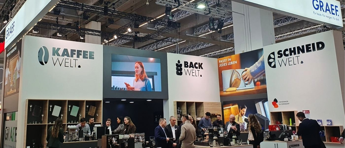Kaffee- und Backwelt-Stand mit Menschen und Werbung für Produkte.