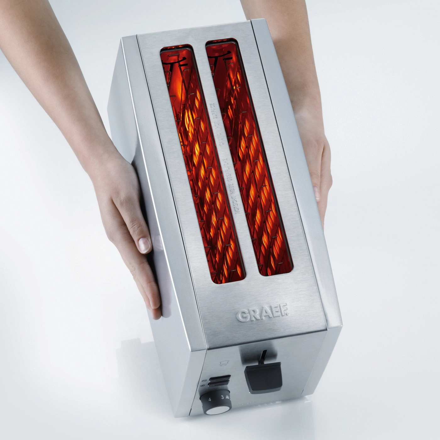 Toaster mit Händen gehalten, Edelstahl, GRAEF-Logo, Toastschlitze, Heizdrähte, Bedienfeld.