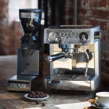 Kaffeemaschine und Kaffeemühle auf einem Holztisch mit Schokoladenkugeln