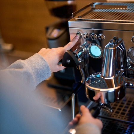 Person drückt Knopf an einer Espressomaschine, um sie einzuschalten.