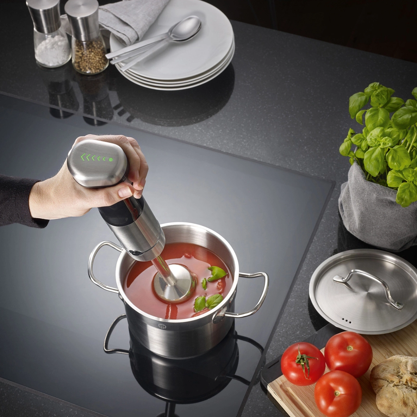 Handmixer in einem Topf mit Tomatensuppe, Basilikum und Tomaten.
