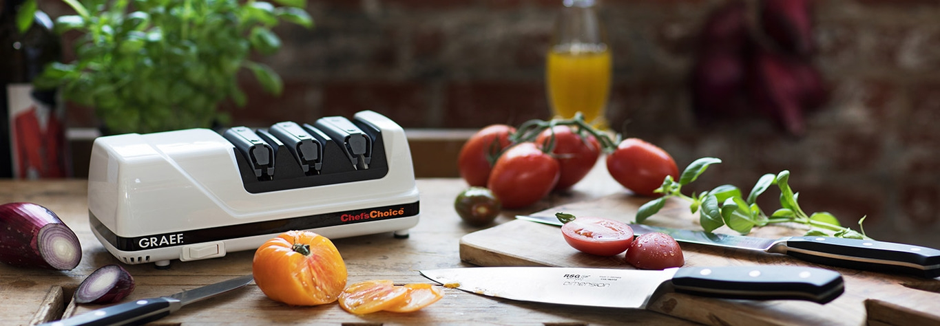 Küchenszene mit Tomaten, Messer, Tomaten, Kräutern und einem Messerschärfer von Chef's Choice.