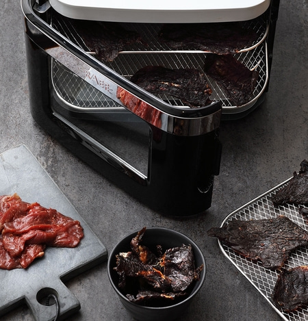 Fleischtrockner mit Fleisch und Trockenfleisch auf grauem Hintergrund
