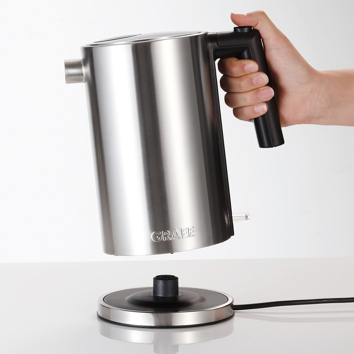 Edelstahl-Wasserkocher, der von einer Hand gehalten wird, über einer Basis.