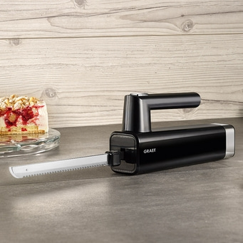 Black electric knife with cake in the background on a gray surface.