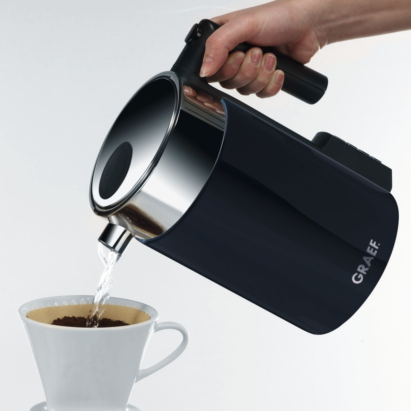 Hand gießt Wasser aus einem Wasserkocher in einen Kaffeefilter mit Kaffeepulver.