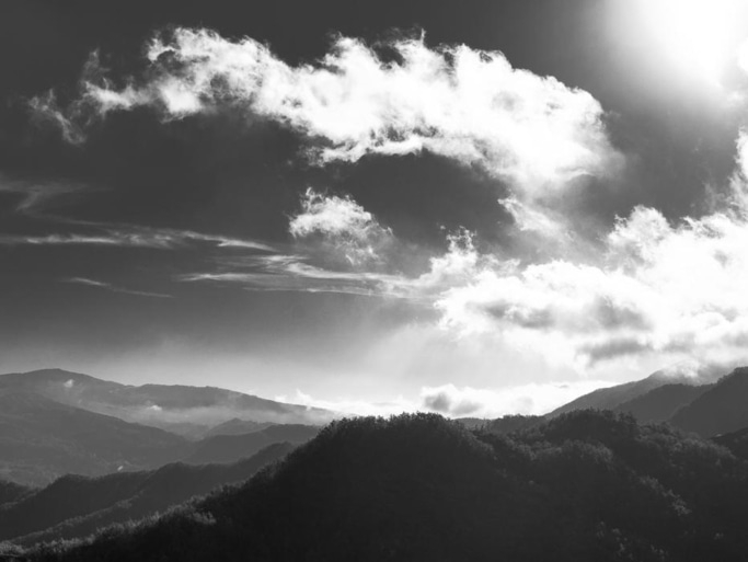 Schwarzweiß-Landschaft mit Bergen und Wolken am Himmel, sonnig