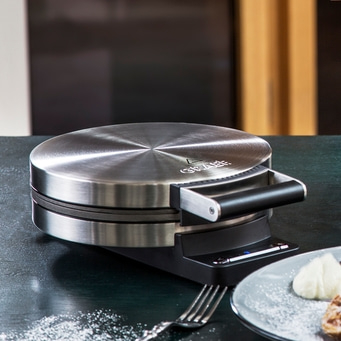 Waffle iron on table with waffle and fork, close-up, stainless steel