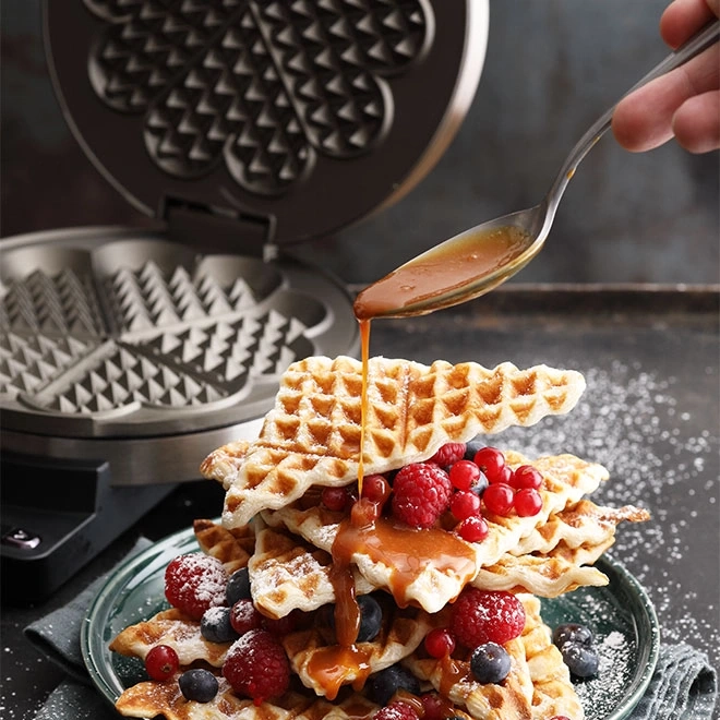 Waffeln mit Beeren und Sirup, die von einer Gabel gegossen werden, mit Waffeleisen.