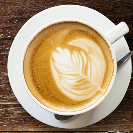 Kaffee mit Latte Art auf einem Unterteller mit Löffel auf Holz